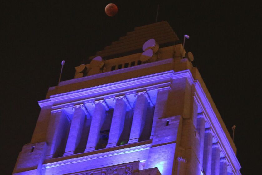 The moon, known as a supermoon due to its slightly closer proximity to Earth, is barely visible in total eclipse over Los Angeles City Hall, one of many iconic area buildings bathed in blue light in support of the L.A. Rams in their NFC championship game Sunday, Jan. 20, 2019. The eclipse came and went as predicted. The Rams defeated the New Orleans Saints and are headed to the Super Bowl. (AP Photo/Reed Saxon)