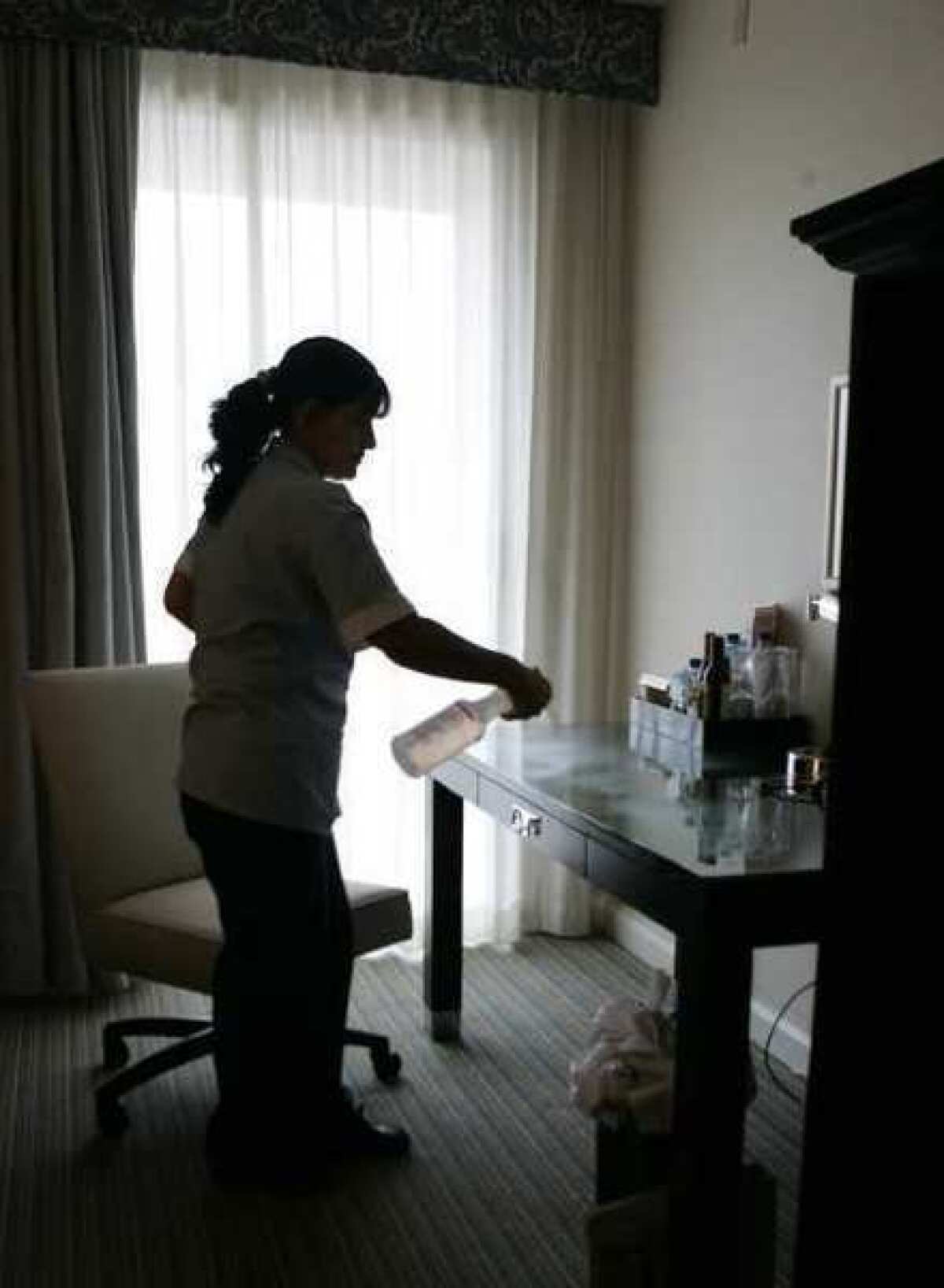 Housekeeper Marina Ortiz sprays cleaner-disinfectant on desk inside a Sheraton hotel room.