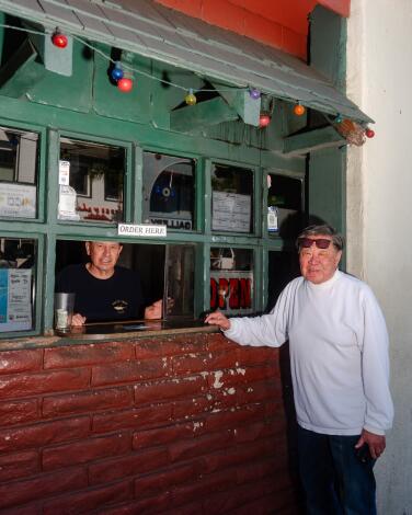 A person stands outside a takeout window, in which another person is visible.