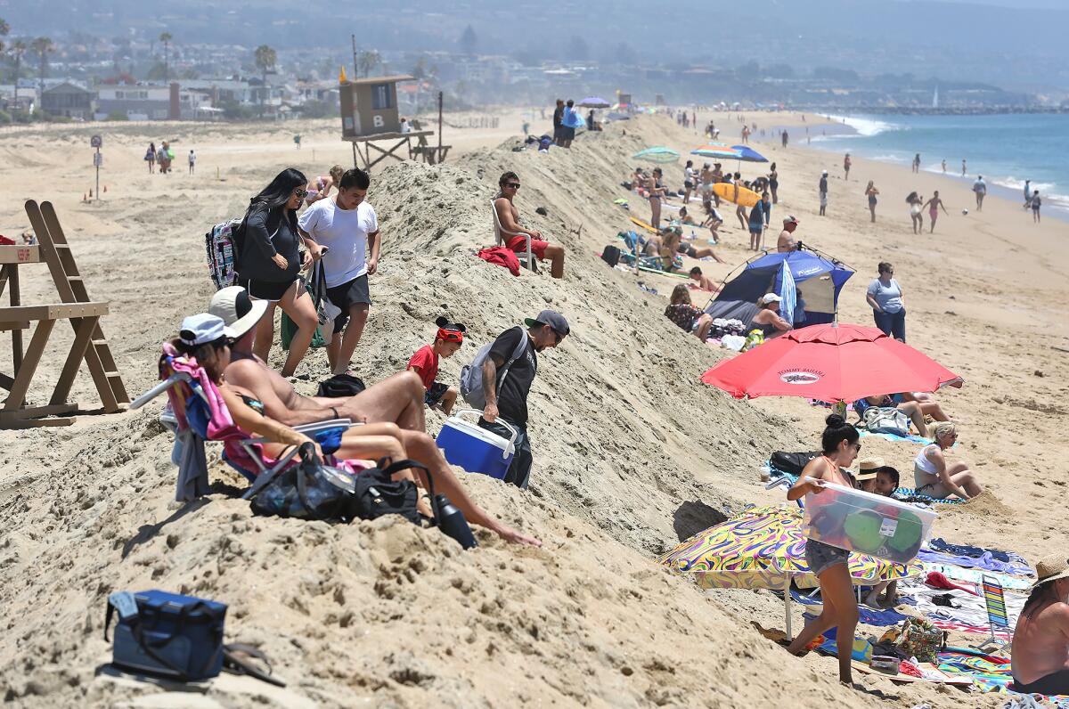 Beach-goers climb a sand berm that was rebuilt by the city to hold off big waves.