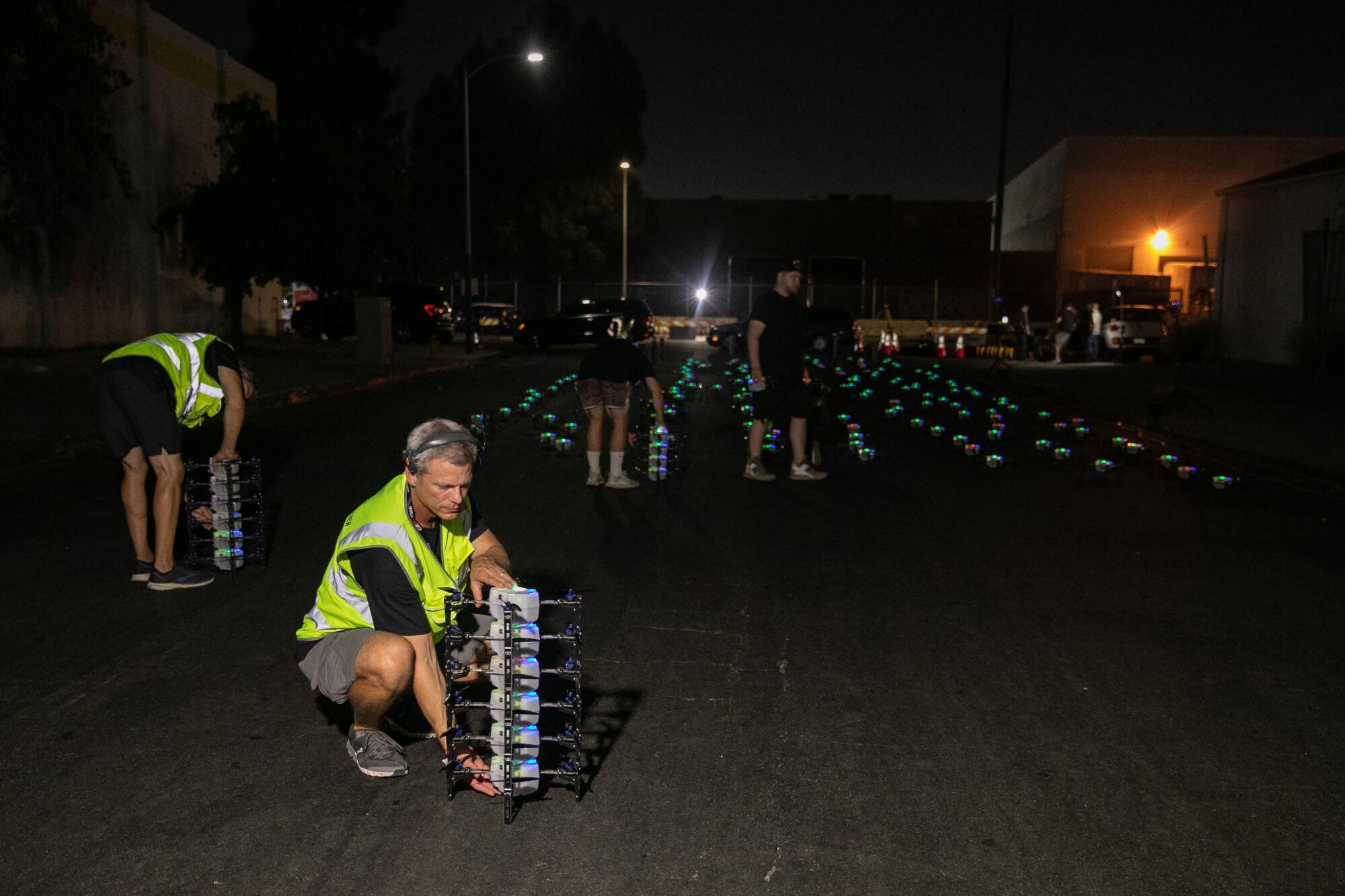 People picking up small drones with lighted drones in rows behind
