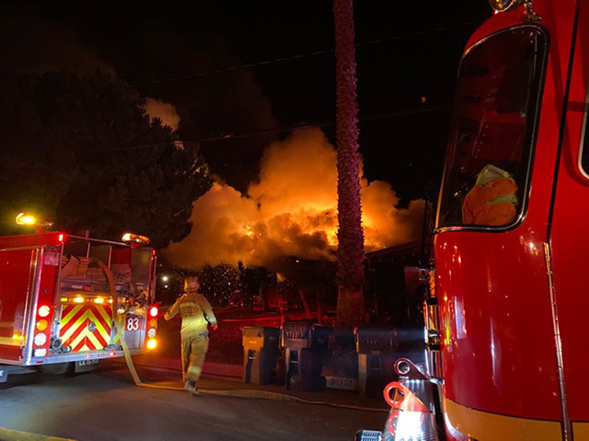 Two firetrucks sit in a street at night as smoke rises in the background.