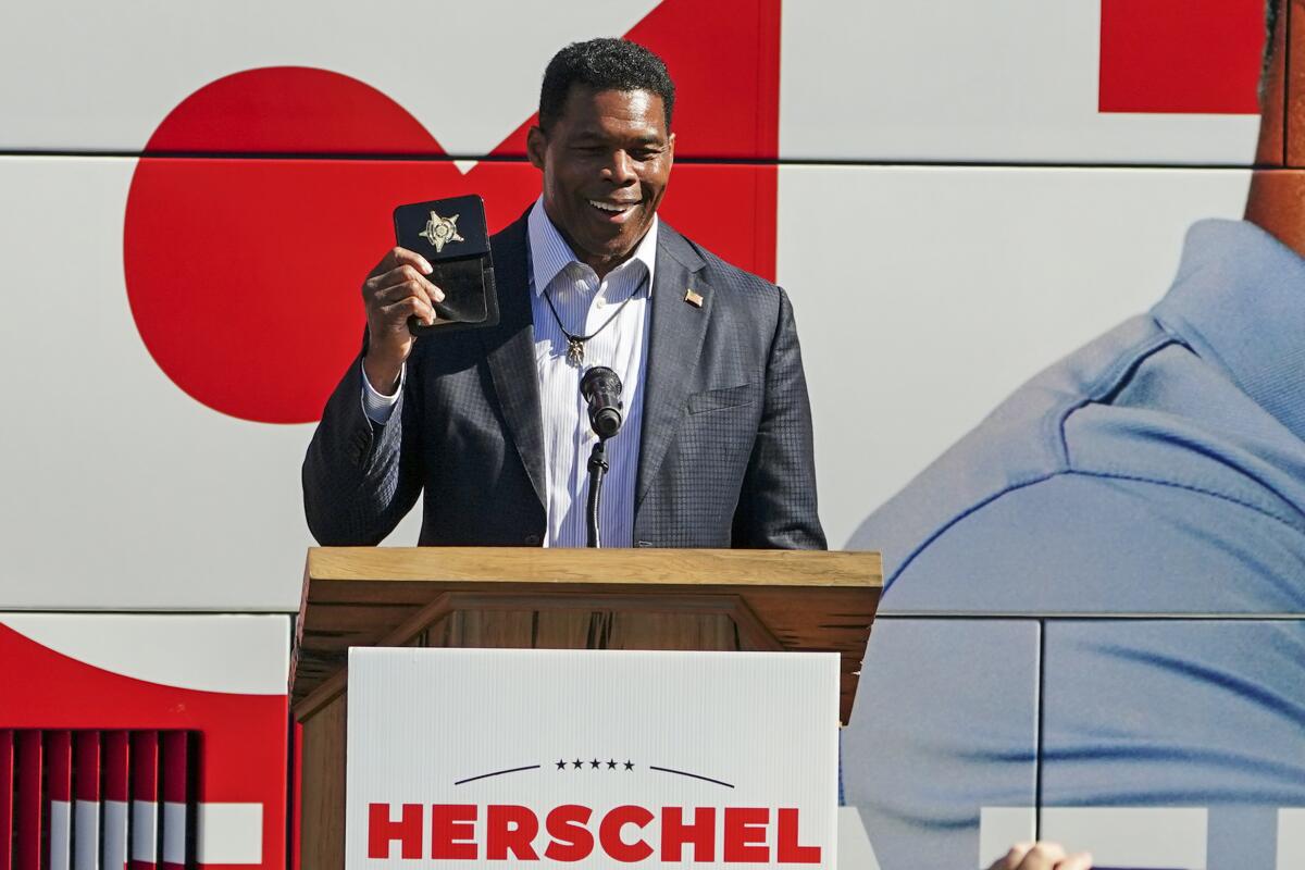  Herschel Walker flashes a badge as he speak to supporters during a campaign rally Oct. 18, 2022, in Atlanta. 