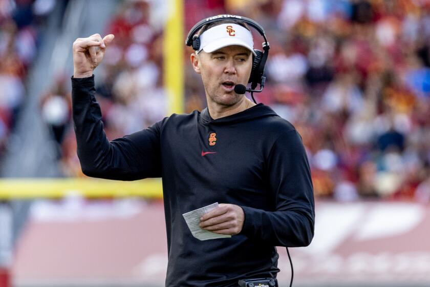 USC coach Lincoln Riley signals up field while holding a card that contains the Trojans' offensive plays 