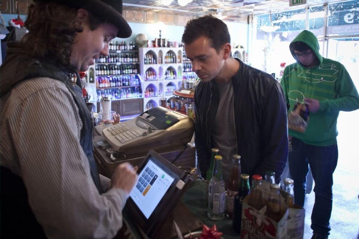 Square founder Jack Dorsey glances over to confirm his identity for a purchase on an iPad running the Square Register app at the Fizzary in San Francisco.