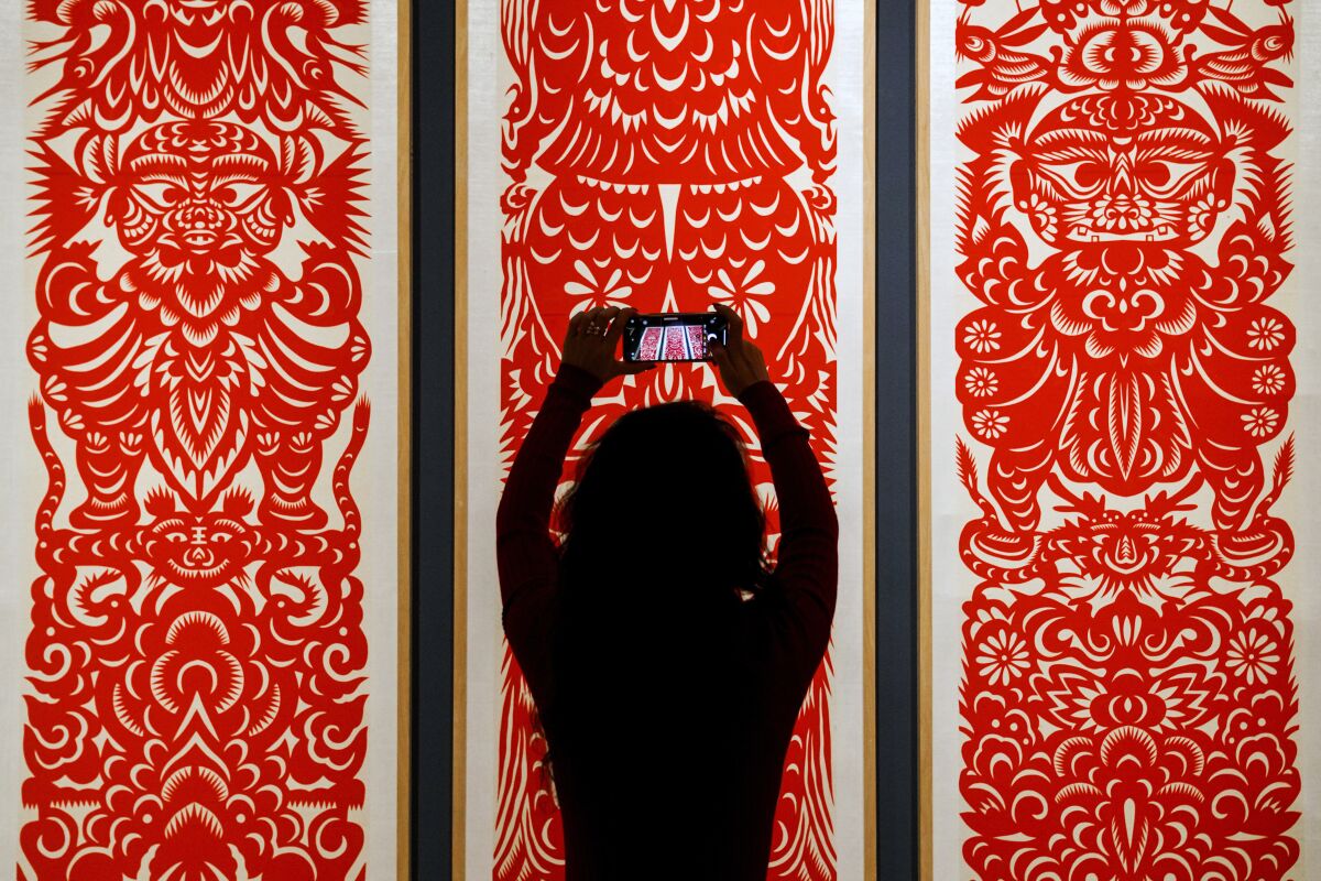 A woman takes a smartphone photo of the Chinese traditional paper cutting arts exhibited at the Beijing Art and Craft Museum during the Lunar New Year celebrations in Beijing, Sunday, Jan. 29, 2023. Chinese people are enjoying a week-long holiday for the Lunar New Year and visiting various temple fairs and exhibitions held in the cities around China. (AP Photo/Andy Wong)