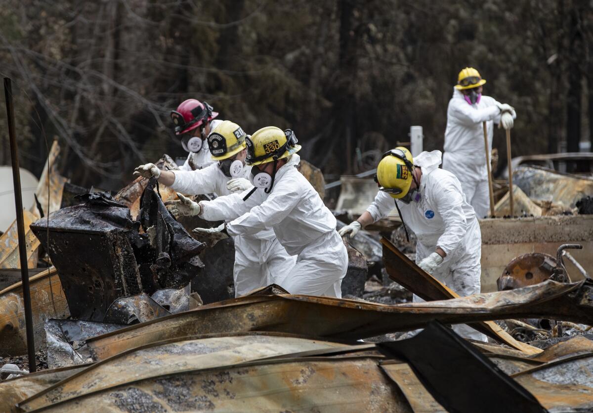 Firefighters move heavy debris while searching for human remains at a destroyed residence 19 days after the Camp fire in Paradise, Calif.