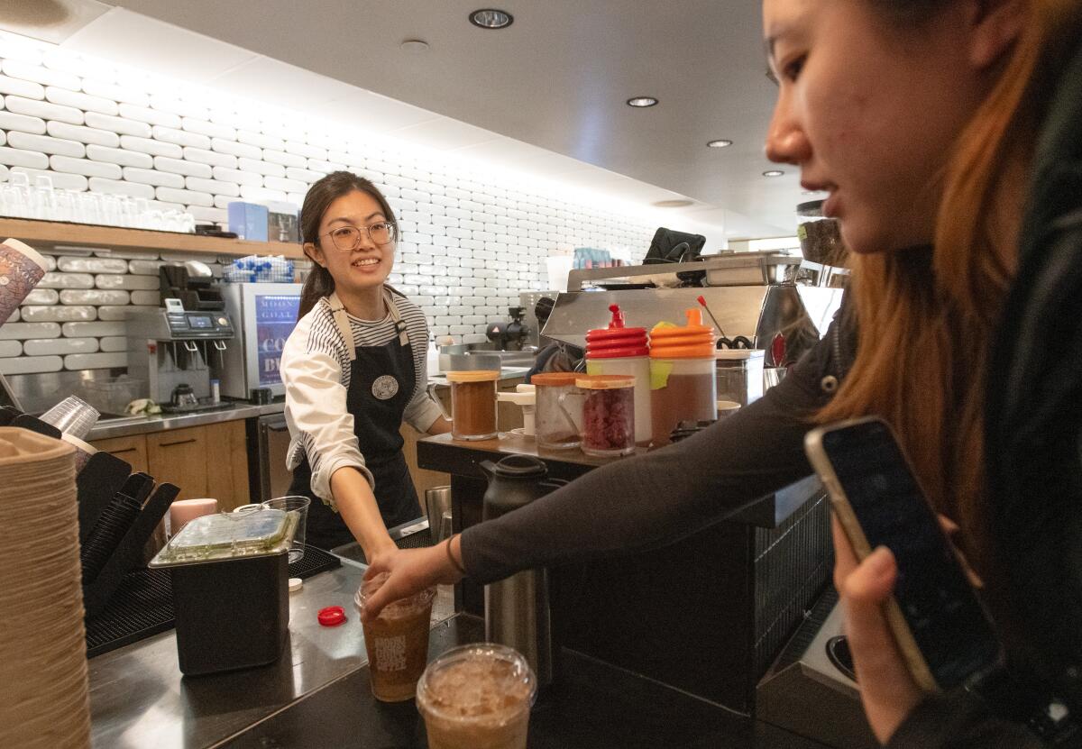 Barista Michelle Chen hands an iced latte to a customer at Moongoat Coffee Roaster's new location.