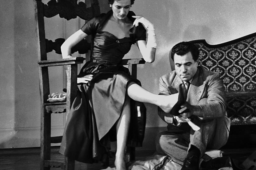 A man. seated on the floor, puts a shoe on a woman's foot in the documentary "Salvatore: Shoemaker of Dreams."