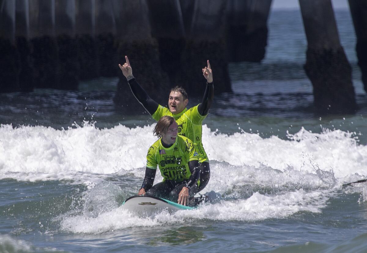Veteran Will McCarthy, front, and Stephen Peterson, U.S. Army specialist, cheer as they ride a wave together.