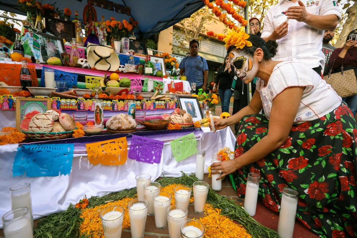A participant lights a candle in front of an altar and its multiple offerings during Noche de Altares in downtown Santa Ana.