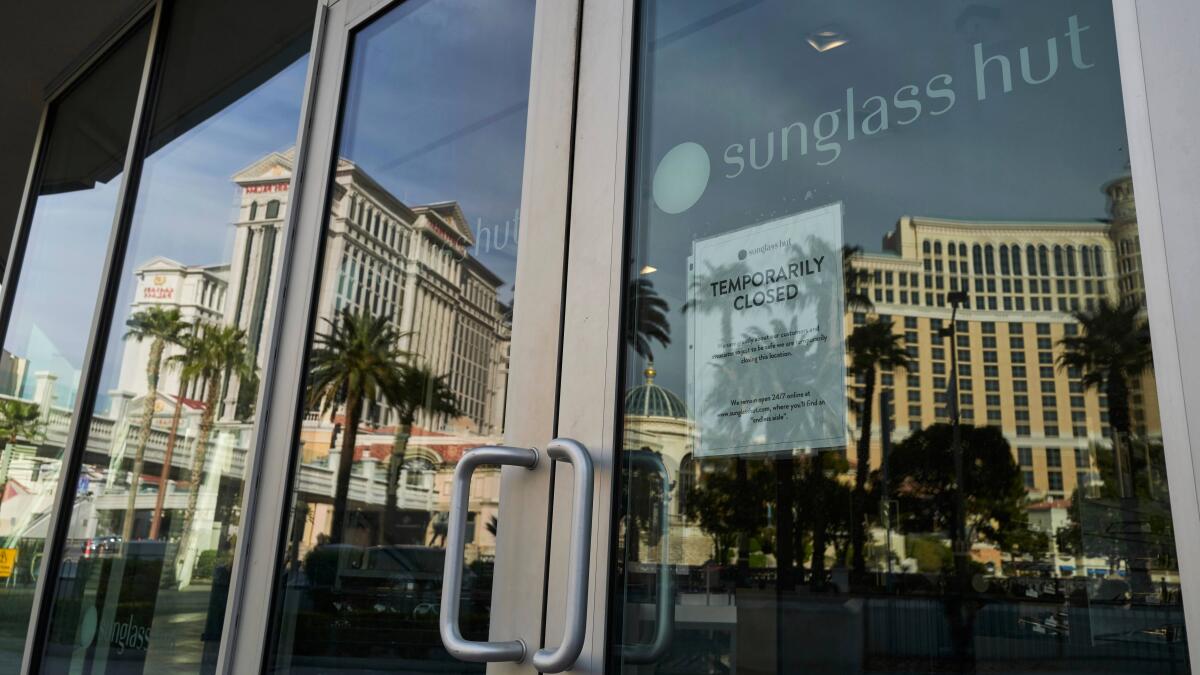 The shuttered Caesars Palace, left, and Bellagio are reflected in the glass doors to a business on the Strip.