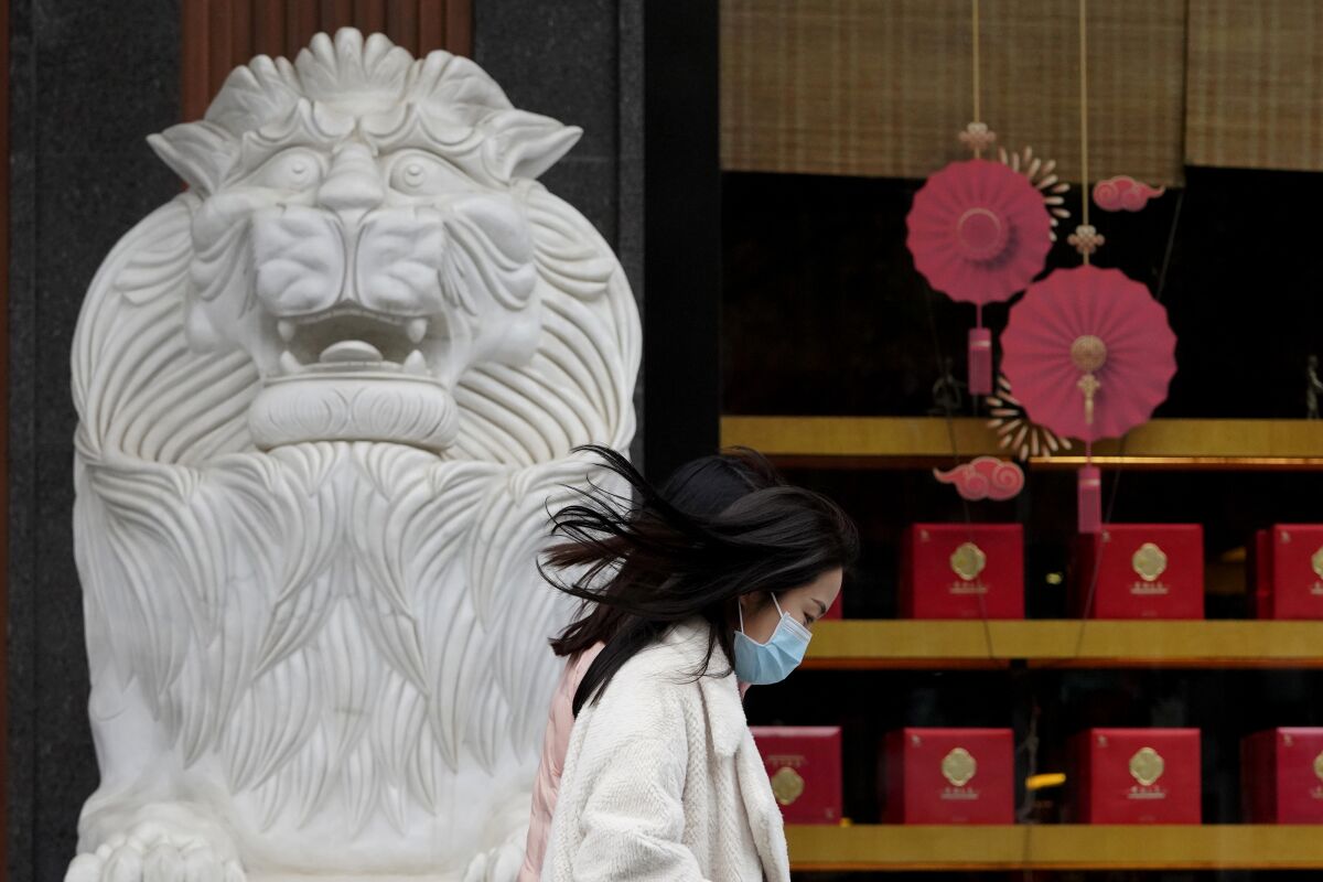 A woman walks past a stone lion and Lunar New Year decorations.
