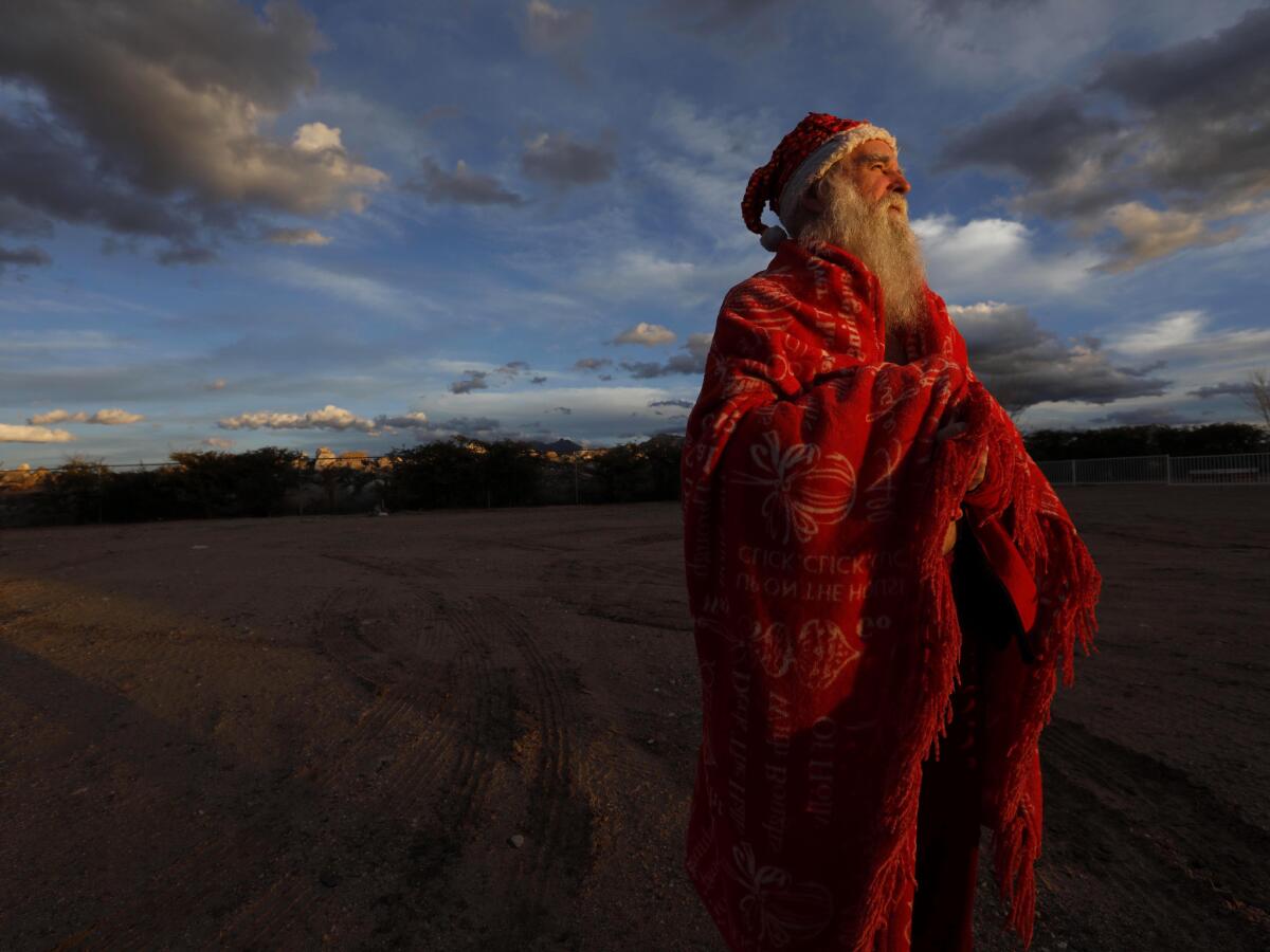 KINGMAN, AZ - MARCH 2, 2019 ? James Zyla, 68, stands in the late afternoon light wrapped in a red blanket across from where he is staying at the Ramada Hotel in Kingman, Arizona on March 2, 2019. Known as Santa James he plays a keyboard at house parties and retirement homes. For years, the white bearded man in the red Santa Claus outfit has been a familiar sight around this isolated high desert town of Kingman, Arizona, his habits so routine that motorists take notice when he isn't there. Zyla had been homeless for years in the community and is currently living in this hotel room. He played piano in the hotel restaurant for free room and board. He no longer plays at the restaurant, but is still allowed to stay at the hotel. (Genaro Molina/Los Angeles Times) ATTENTION PRE-PRESS: PHOTO WAS MADE IN LATE AFTERNOON LIGHT. PLEASE MAINTAIN COLOR AND TONE. PLEASE DO NO LIGHTEN. TRY AND MATCH THIS SCAN. THANKS.