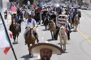 Horse riders make their way down a street, some carrying U.S. and Mexican flags