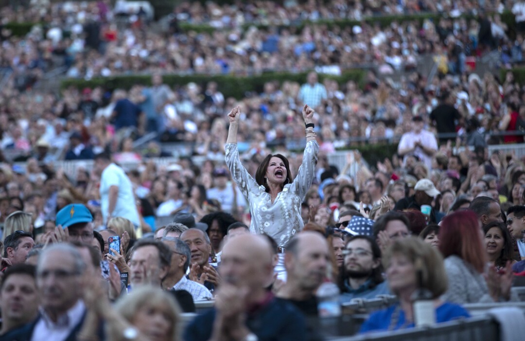 A person stands, raising both arms and shouting, amid a sold-out crowd.