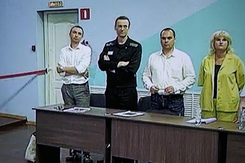 Russian opposition leader Alexei Navalny, 2nd left, is seen on a TV screen standing among his lawyers, as he appears in a video link provided by the Russian Federal Penitentiary Service, during a hearing in the colony, in Melekhovo, Vladimir region, about 260 kilometers (163 miles) northeast of Moscow, Russia, on Friday, Aug. 4, 2023. Navalny on Friday was convicted on extremism charges and sentenced to 19 years in prisons, in the harshest ruling against the imprisoned Kremlin critic to date. (AP Photo/Alexander Zemlianichenko)