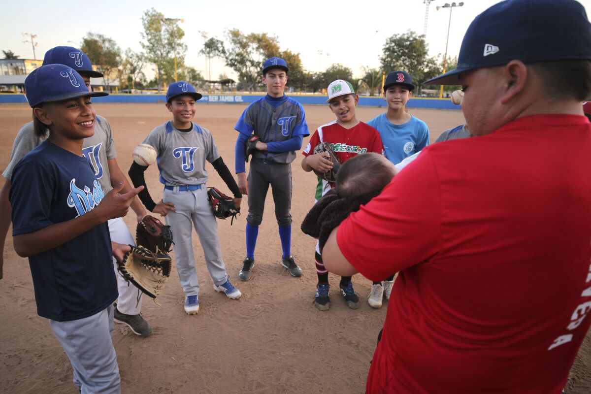 Municipal de Tijuana coach Victor Rivera holds his baby son Alejandro as he talks to his players during practice at the Liga de Beisbol Infantil y Juvenil Municipal de Tijuana on Friday, July 26, 2019 in Tijuana , Mexico.