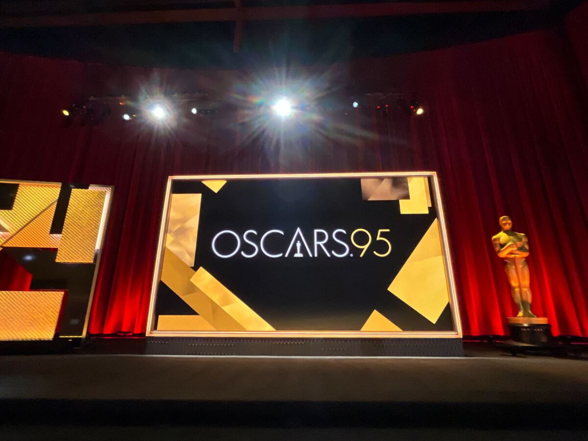 A large Oscar statuette stands onstage beside a screen that says Oscars 95.