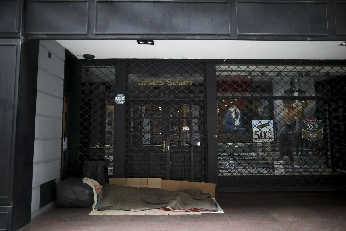 A homeless man sleeps in front of a store at the financial district during a government-ordered lockdown to curb the spread of COVID-19 in Buenos Aires, Argentina, Thursday, May 21, 2020. Friday is the deadline for Argentina to reach an agreement with its bondholders about a restructuring of the debt. If bondholders do not accept the Argentine offer or the country does not pay interest due May 22, Argentina will default on its debt for the ninth time in its history. (AP Photo/Natacha Pisarenko)