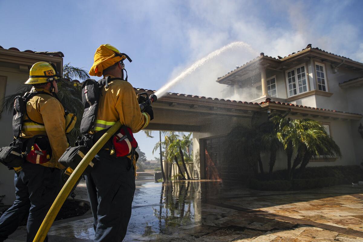 El Segundo firefighters Mathew Goodenough, left, and Javier Olmeda hose down a smoldering home in Laguna Niguel on Thursday.