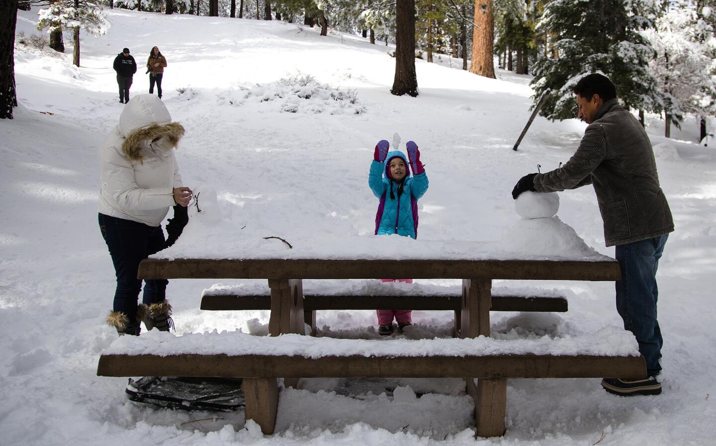 Jennifer and Carlos Rodriguez of Wrightwood with daughter Tiffany, 8, build snowmen on snow-covered picnic tables at a recreation area off Highway 2 after the recent storm dumped needed snow in the mountains on Dec. 17.