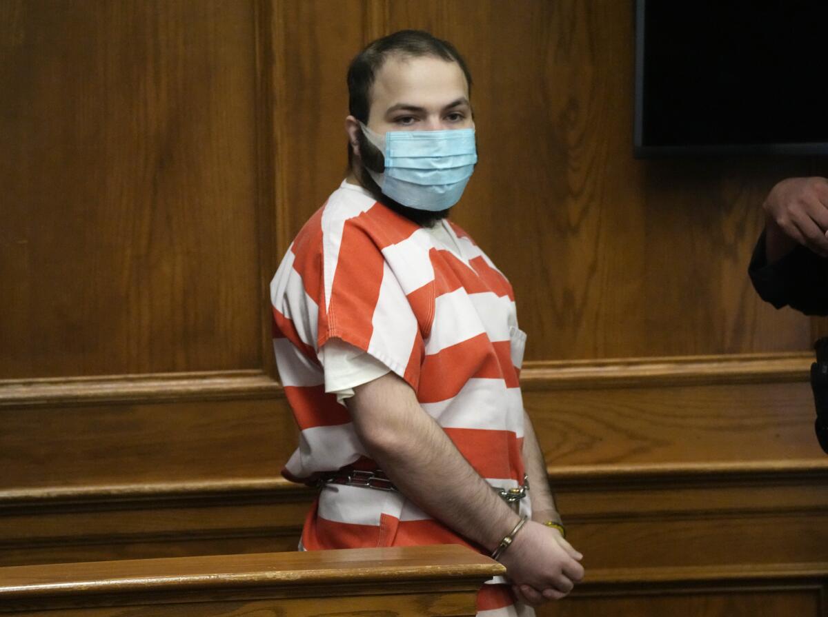 A shackled man in a striped prison uniform stands in a courtroom.
