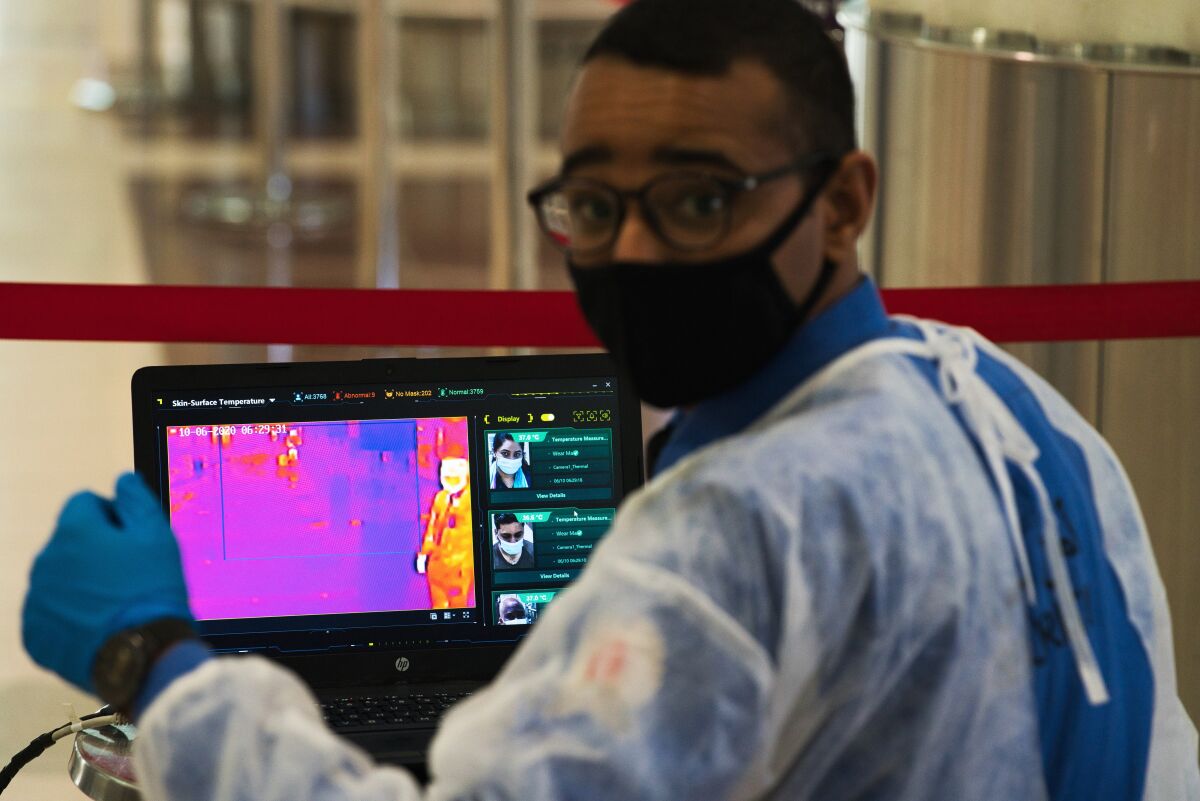 FILE - In this June 10, 2020 file photo, an official wearing a mask due to the coronavirus pandemic operates a temperature screening point at Dubai International Airport's Terminal 3 in Dubai, United Arab Emirates. Efforts by the United Arab Emirates to fight the coronavirus have renewed questions about mass surveillance in this U.S.-allied federation of seven sheikhdoms. (AP Photo/Jon Gambrell, File)
