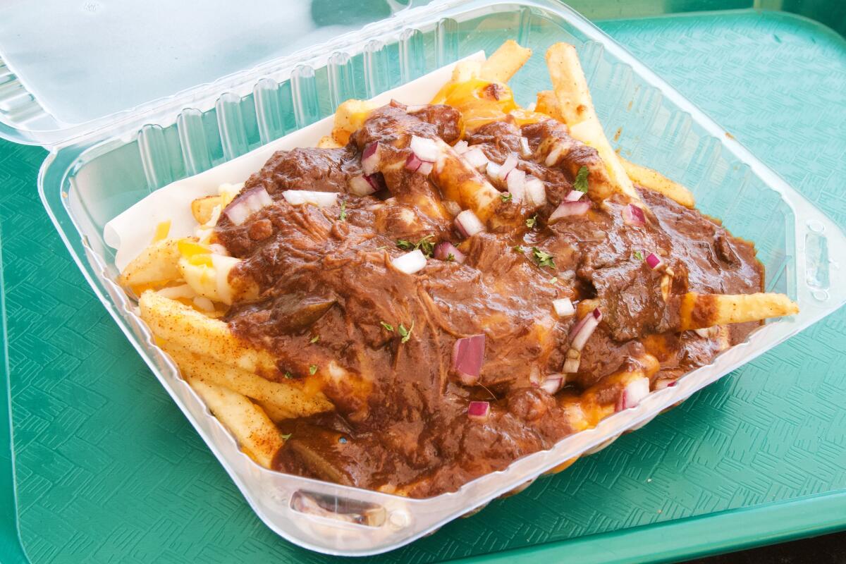 A side view of debris gravy cheese fries in a plastic to-go container on a green tray from Little Jewel of New Orleans