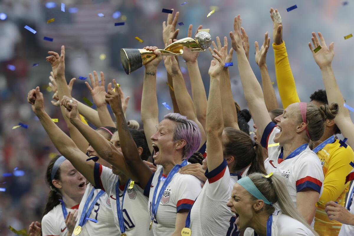 Megan Rapinoe holds up a trophy surrounded by excited teammates