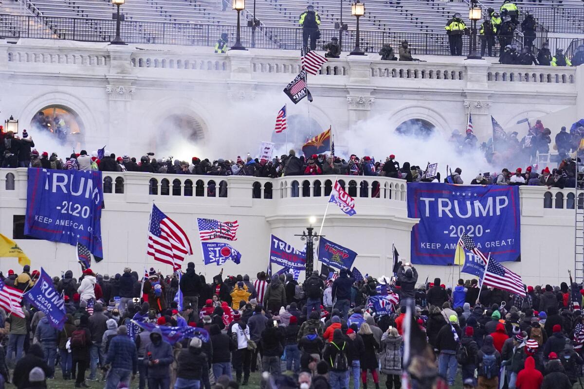 Rioters with Trump banners and American flags amid smoke outside the U.S. Capitol