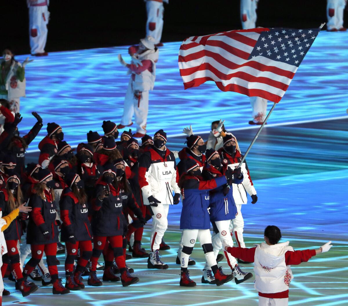 Two people hold the U.S. flag at the 2022 Olympics while a group follows them