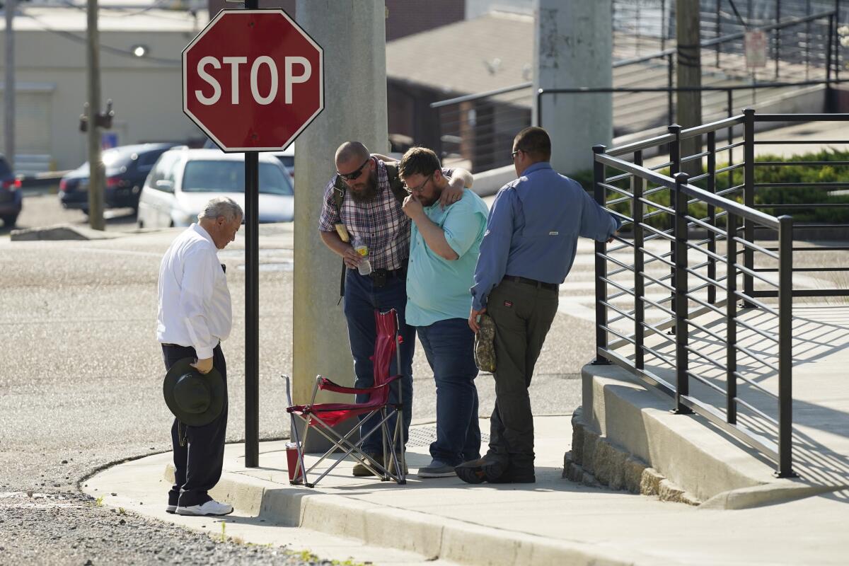Men bow their heads in prayer standing on a curb next to a stop sign