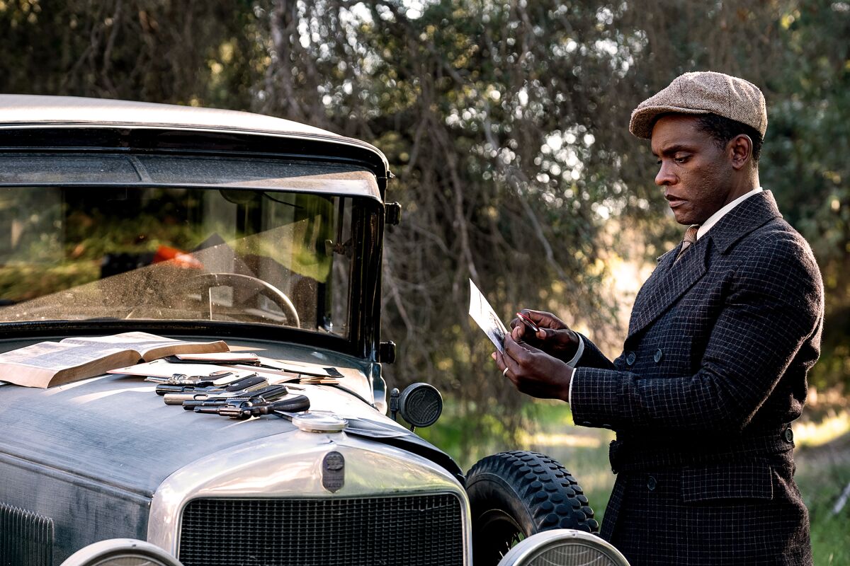 Chris Chalk as Paul Drake stands in front of a car with guns on the hood in "Perry Mason."
