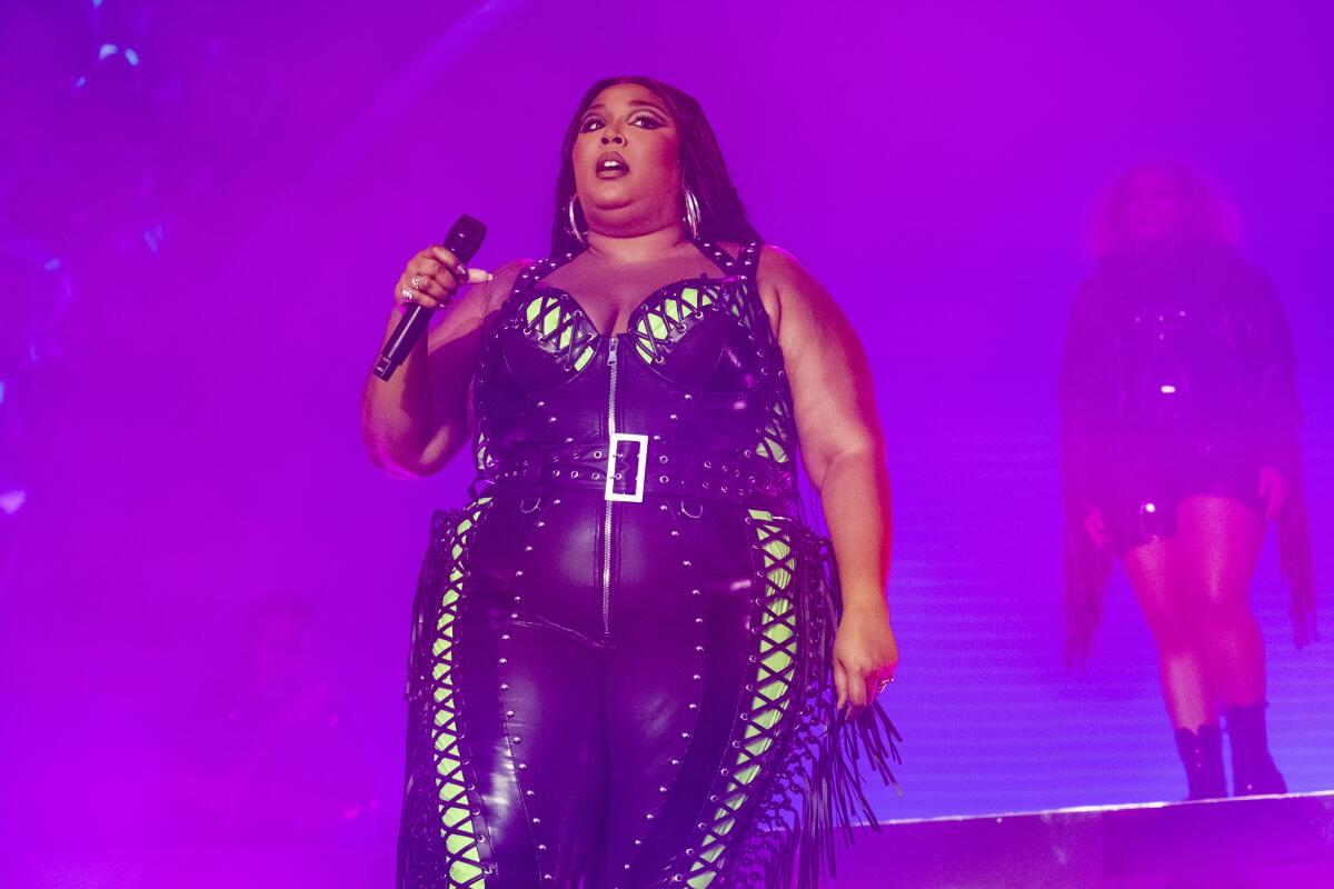 Lizzo wears a black leather outfit with yellow accents as she performs onstage