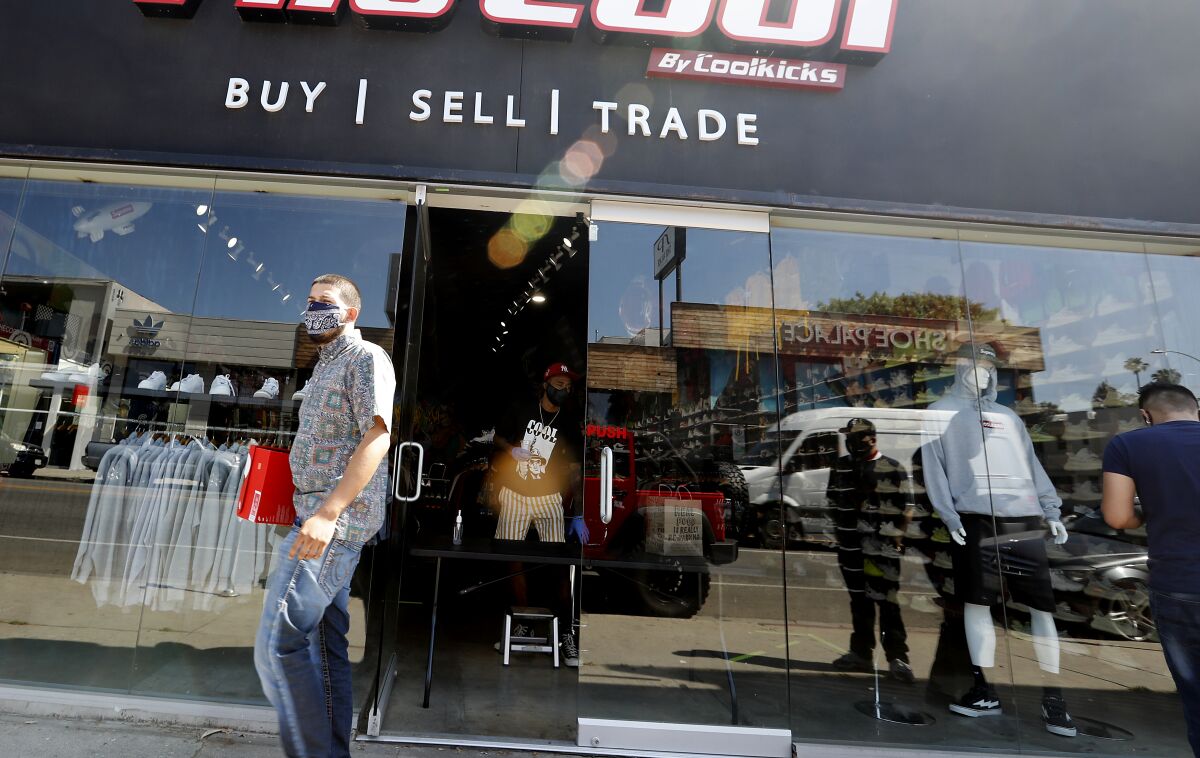 A customer picks up a purchase at the front door of a sports shoe and apparel store along Melrose Avenue in Los Angeles on Friday, following the curbside pickup and social distancing rules.