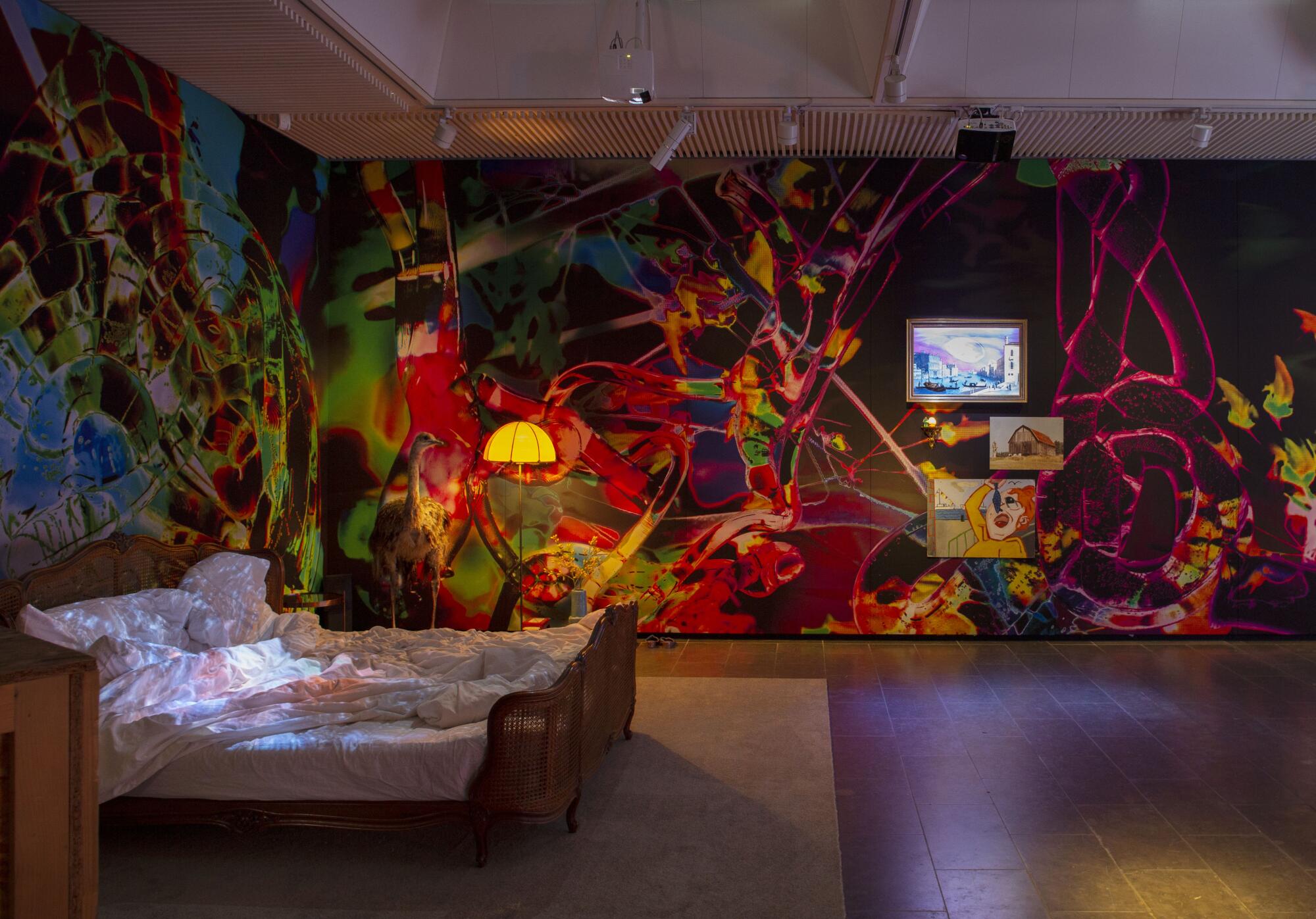 A gallery view shows a bed with video projections and walls covered in wallpapers that evoke dense vegetation
