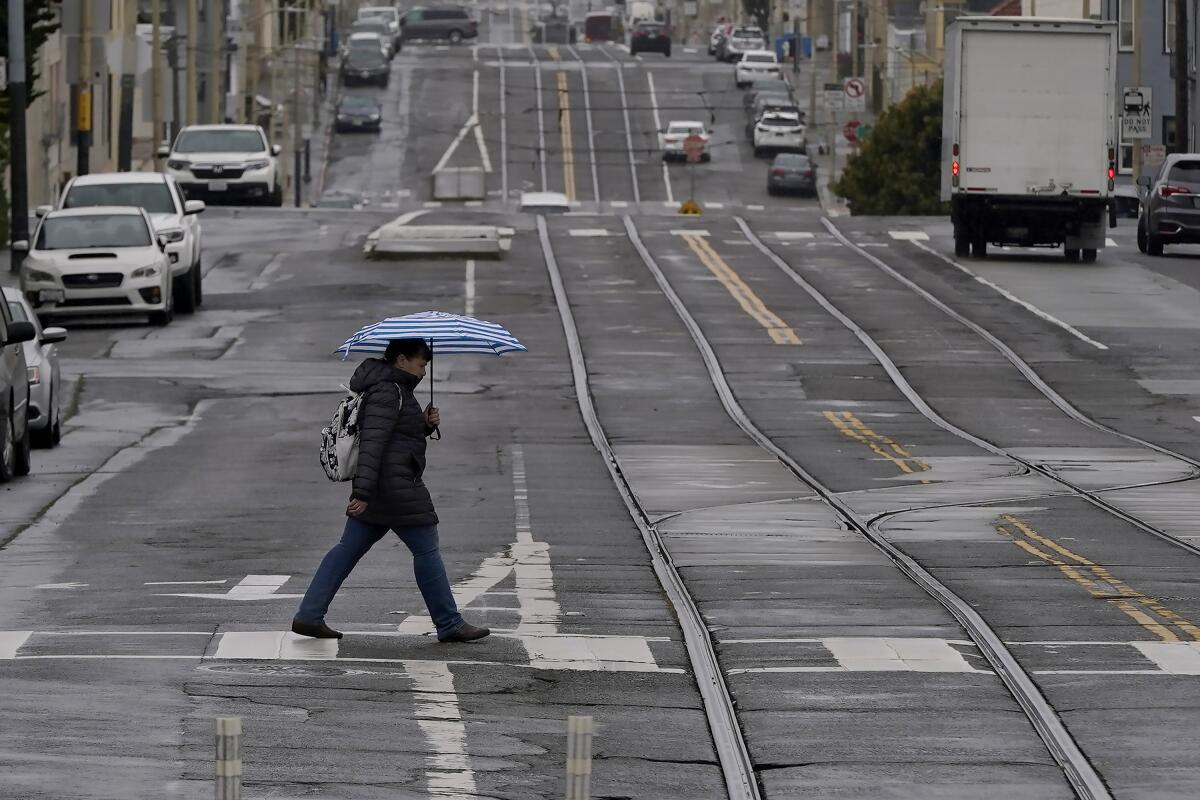 A pedestrian carries an umbrella while crossing a street in San Francisco.