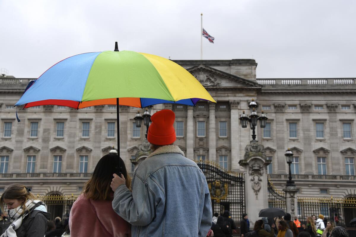 A couple under an umbrella look at the Union flag at half-staff over Buckingham Palace in London, a day after the death of Britain's Prince Philip, Saturday, April 10, 2021. Britain's Prince Philip, the irascible and tough-minded husband of Queen Elizabeth II who spent more than seven decades supporting his wife in a role that mostly defined his life, died on Friday. (AP Photo/Alberto Pezzali)