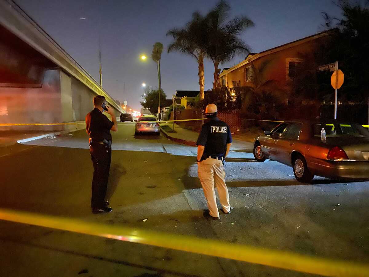 Officers stand inside yellow crime tape at the site of a fatal shooting of a 17-year-old in South L.A.