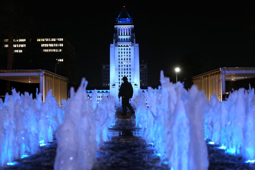 LOS ANGELES, CA - JANUARY 08, 2021 - A security officer is framed by Los Angeles' City Hall lit in Dodger blue tonight and through the weekend to honor the loss of former Los Angeles City Councilmember Tom LaBonge and Dodgers legend Tommy Lasorda as seen from Jerry Moss Plaza in Los Angeles on January 8, 2021. The blue cast on City Hall was requested by City Council President Nury Martinez and Mayor Eric Garcetti, according to Martinez' office. (Genaro Molina / Los Angeles Times)
