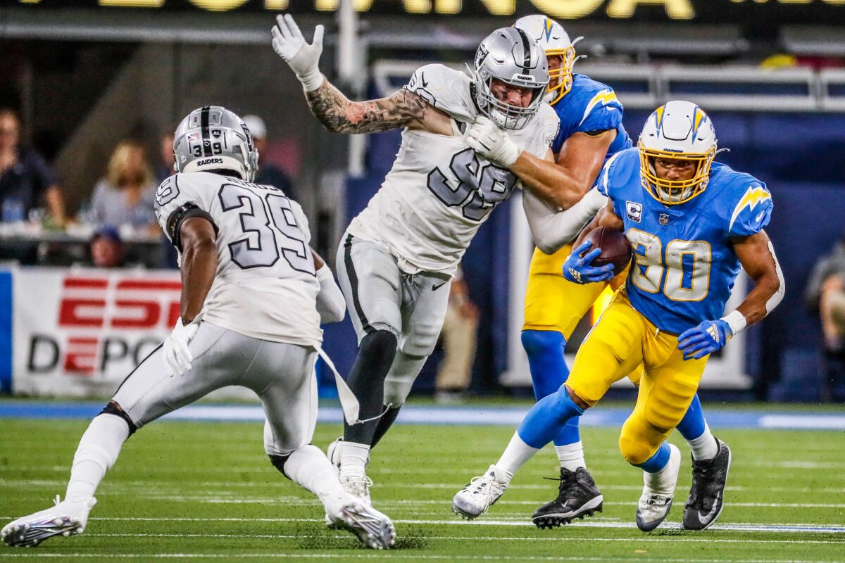 Chargers running back Austin Ekeler (30) eludes Raiders Clelin Ferrell (99) and Nate Hobbs (39) in October. 