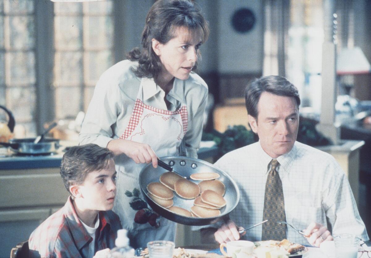 Frankie Muniz, left, and Bryan Cranston, right, set at a kitchen table as Jane Kaczmarek serves pancakes.