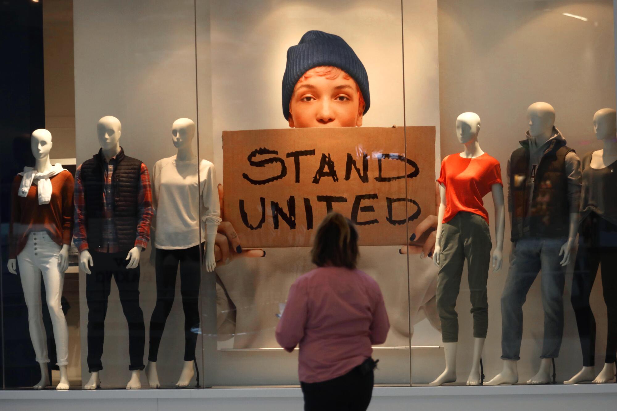 A woman looks at a window display including a sign saying "Stand United."
