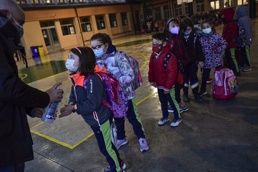 A group of young students wearing face mask protection to prevent the spread of the coronavirus disinfect their hands while waiting in a queue before entering the Luis Amigo school after Christmas holidays, in Pamplona, northern Spain, Monday, Jan. 10, 2022. Spanish health authorities try to control high incidence curve of COVID-19.(AP Photo/Alvaro Barrientos)