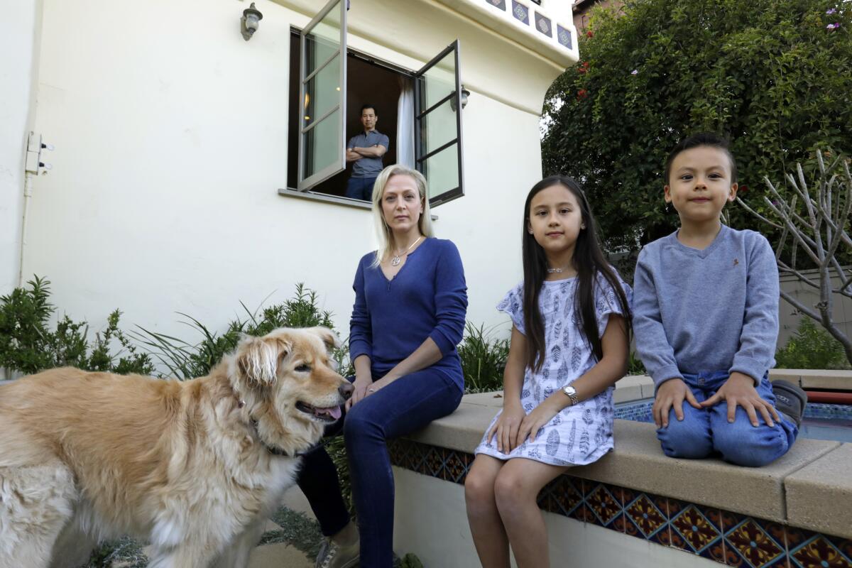 Oral surgeon Kevin Lew, in window, went into self-isolation in his Los Feliz home as soon as he developed symptoms from the coronavirus. His wife, Astrid, wore a mask and gloves when she took him food. Their two children, Brandon, 6, right, and Eva, 9, couldn't visit him.