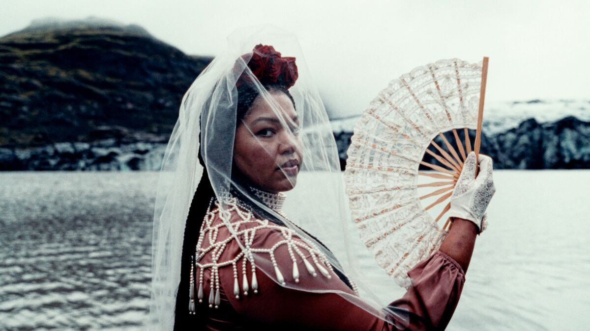 A woman looks into the camera while holding up a fan