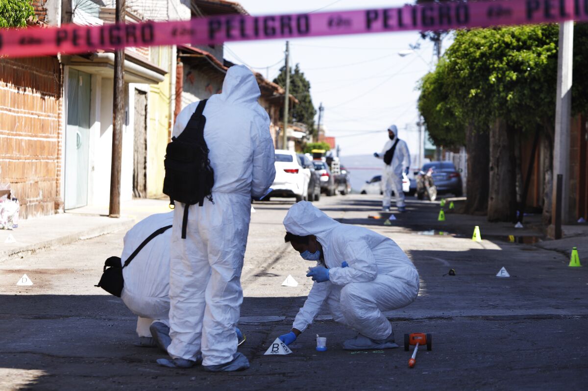 Investigators comb the site where more than a dozen people were believed to have been gunned down by armed men on Sunday, in San Jose de Gracia, head of the municipality of Marcos Castellanos, in Michoacan state, Mexico, Monday, Feb. 28, 2022. In a video apparently shot by a resident and posted on social media, men were lined up against a wall by drug cartel gunmen toting assault rifles. Prosecutors said they can't say how many died, because the attackers cleaned up the scene, washed the sidewalk and carted away any bodies. (AP Photo/Armando Solis)