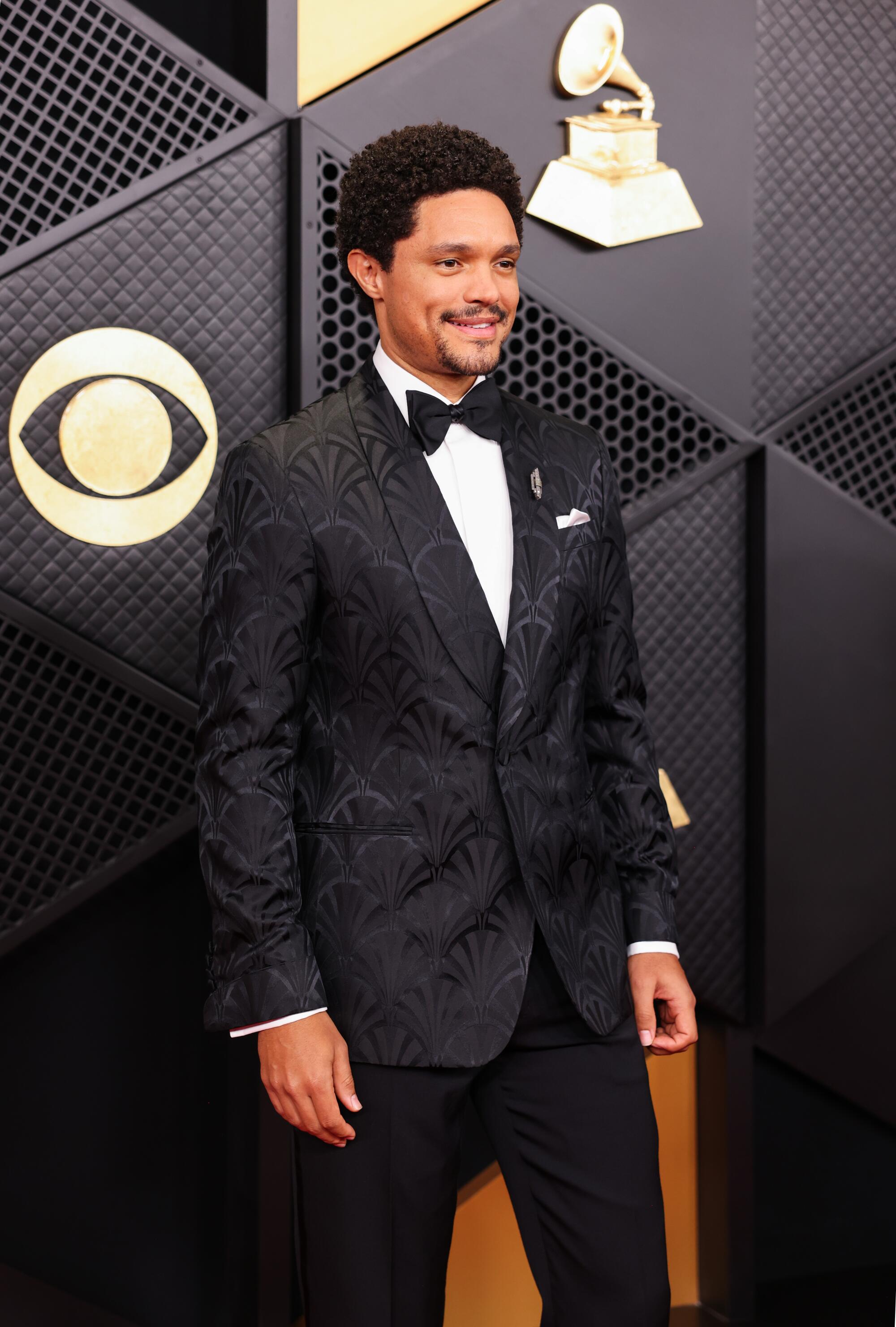 Trevor Noah, wearing a textured suit, poses on the red carpet.