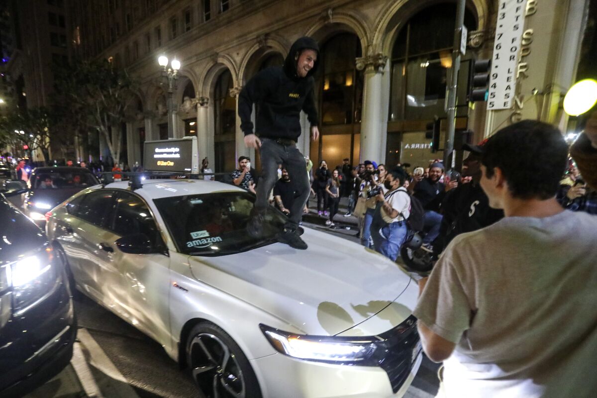A man jumps on top of a vehicle as football fans celebrate the Los Angels Rams winning Super Bowl LVI football